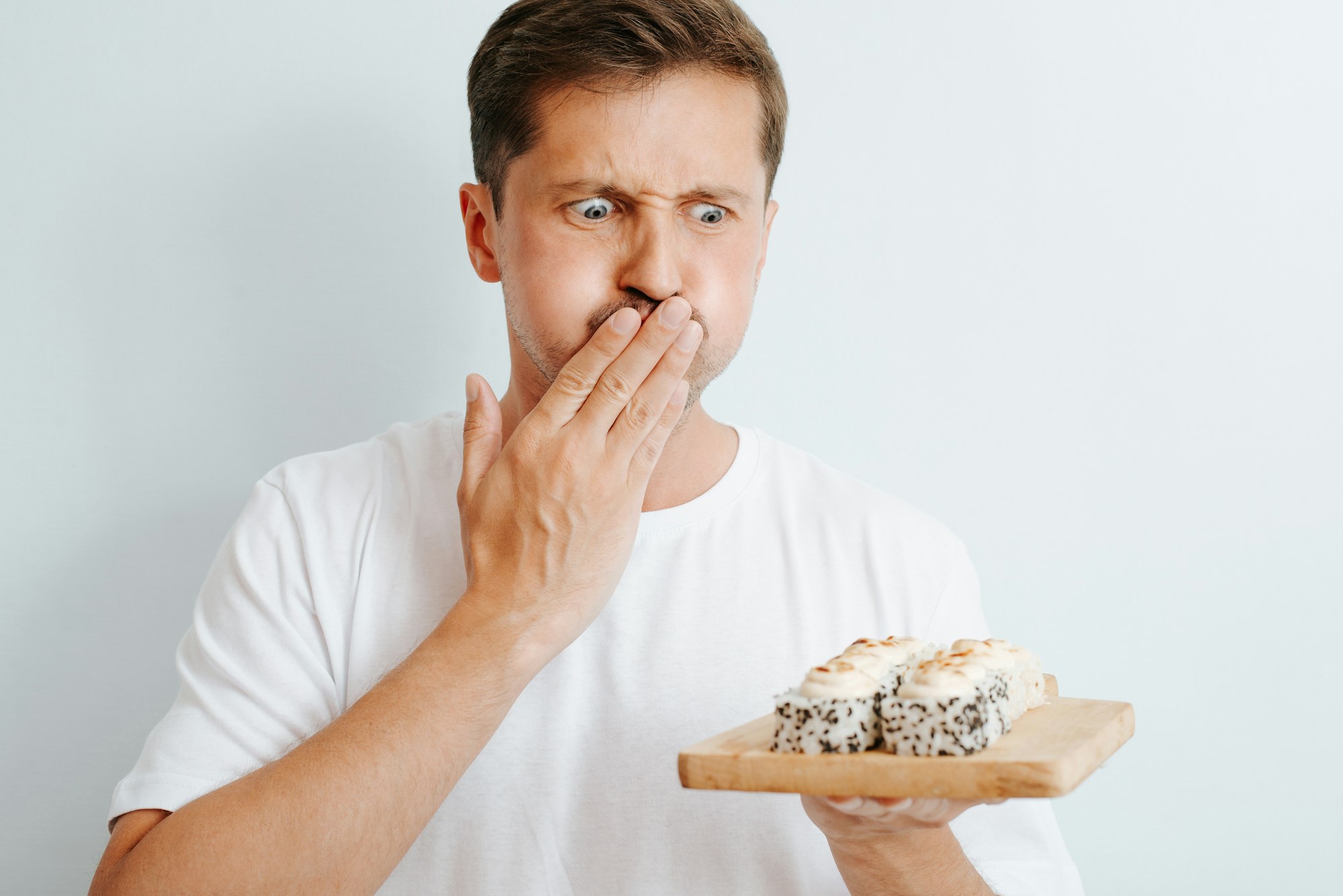 Sick guy with symptoms of nausea and food poisoning looking at sushi indoors.